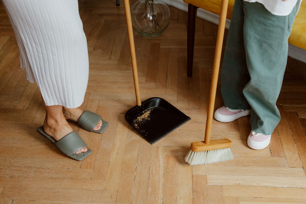 about-img A mother and child cleaning the floor with a broom and dustpan indoors.