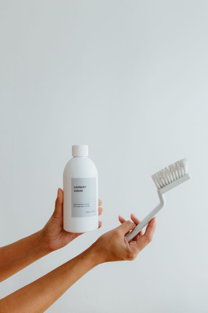 why-choose-us Close-up of hands holding a laundry liquid bottle and cleaning brush on a white background.